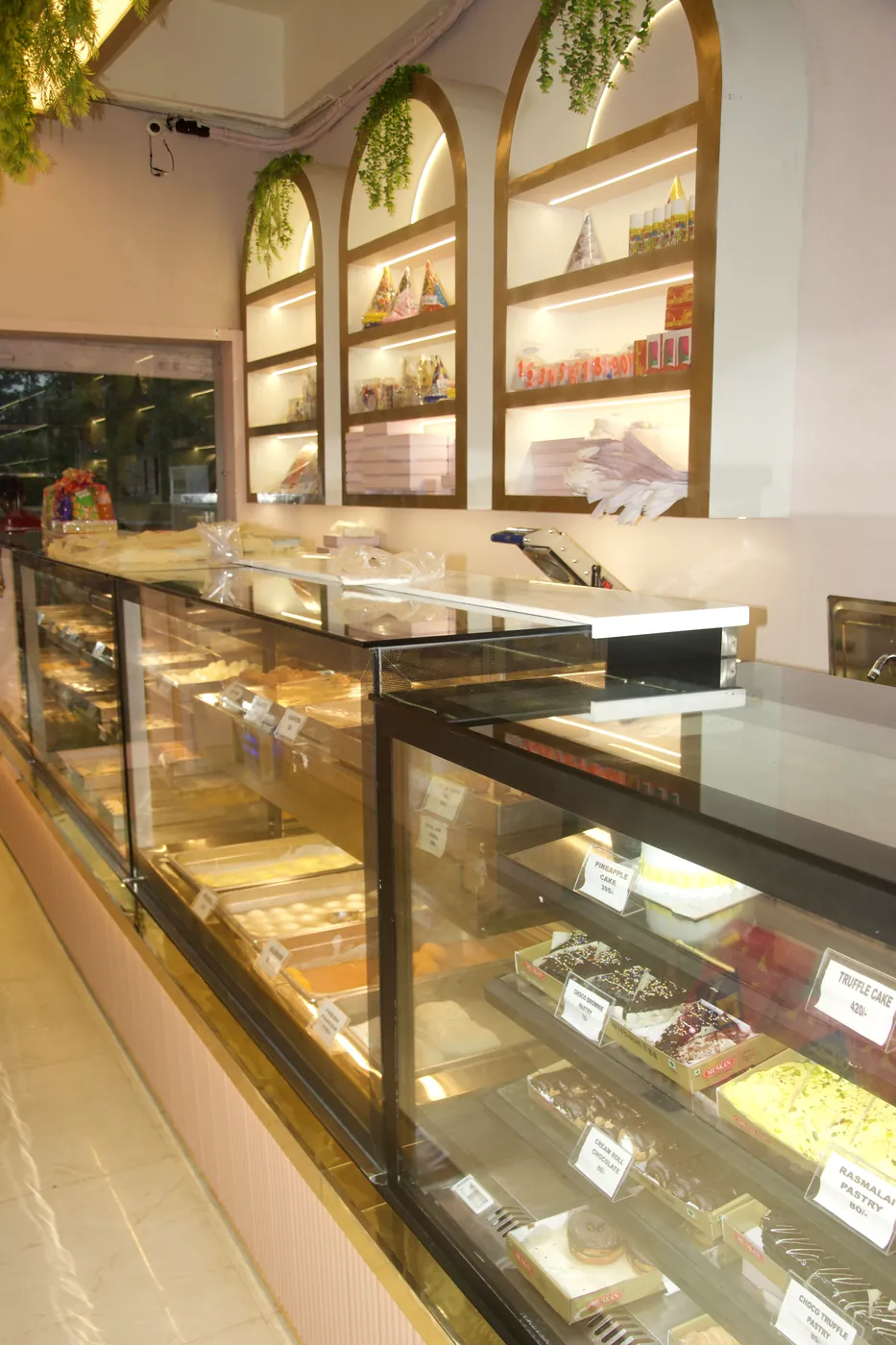 Mithai counter with fresh Indian sweets under brass arches at Noida Sweets and Bakers, Greater Noida